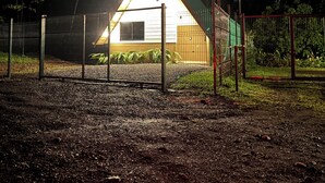 Un edificio triangular con una luz brillante en la parte superior, rodeado por una cerca metálica y árboles.