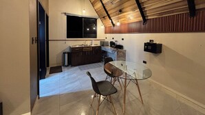 Una cocina moderna con una mesa de comedor de vidrio y sillas, vigas de techo de madera y un ventanal sobre el fregadero.