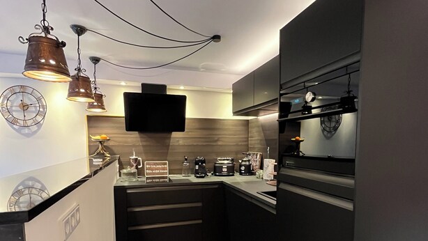 A modern kitchen with a black countertop, a built-in oven, and a flat-screen TV mounted above the stove. - Späth Business Apartment Furnished 2-room basement in Schwanstetten (Schwanstetten)