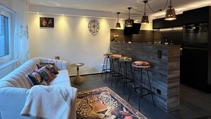 A modern living room with a sofa, a patterned rug, and a kitchen area with bar stools. - Späth Business Apartment Furnished 2-room basement in Schwanstetten (Schwanstetten)