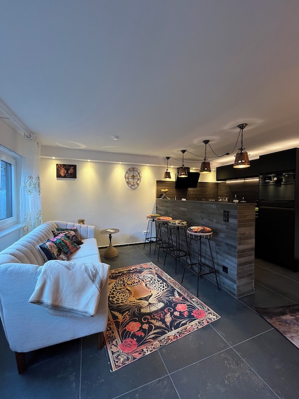 Ein modernes Wohnzimmer mit einer Couch, einem gemusterten Teppich und einer Küchenzeile mit Barhocker.