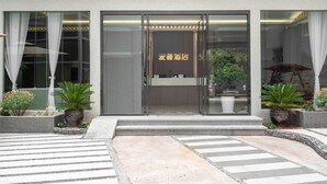 A hotel entrance with a glass door, potted plants, and a clear view of the interior. - Ancient City District Ai Shan Hotel (Lijiang)