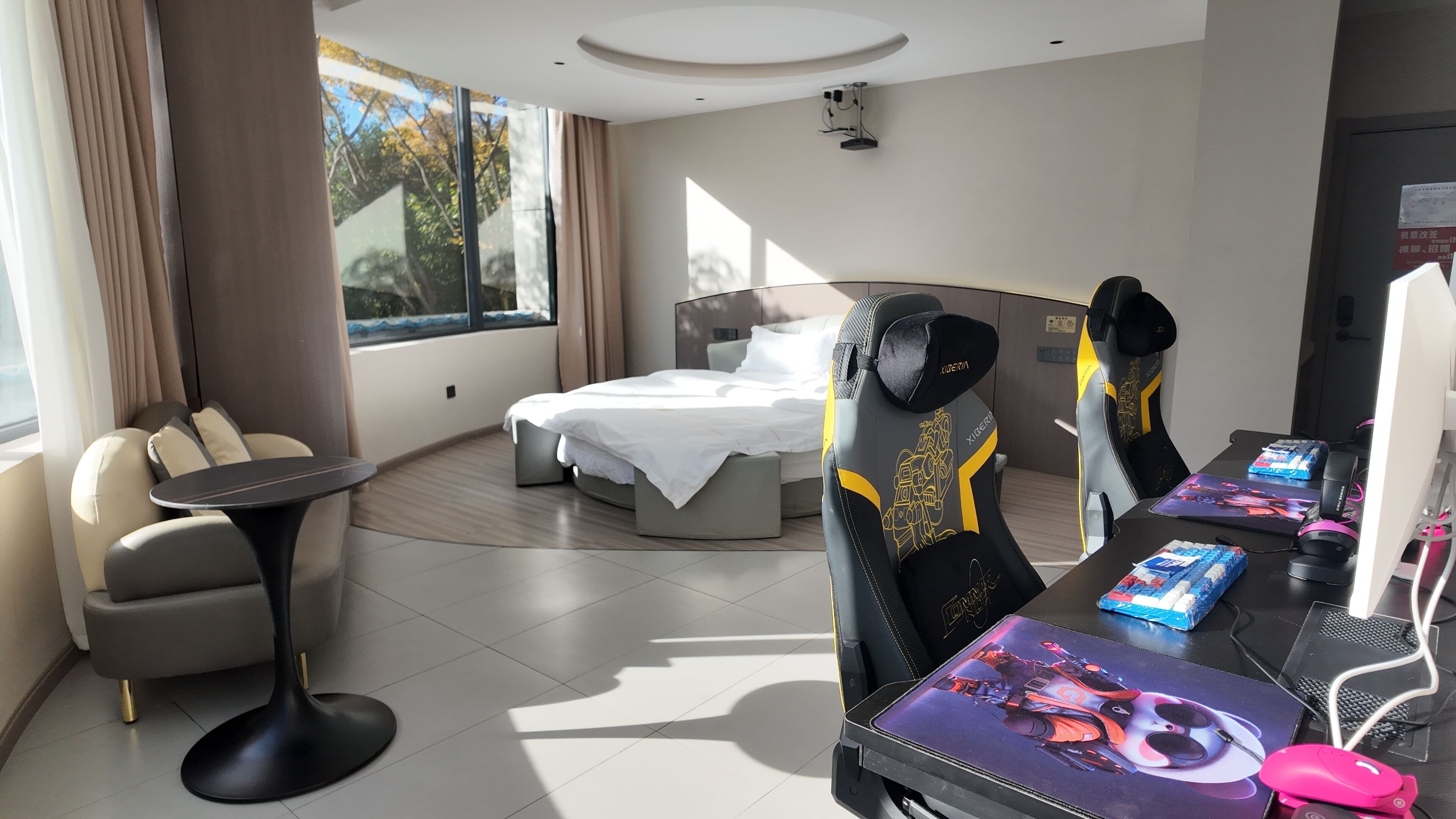 Une chambre d’hôtel moderne équipée d’un lit, d’un bureau avec un ordinateur, et d’un coin salon comprenant une chaise et une petite table.
