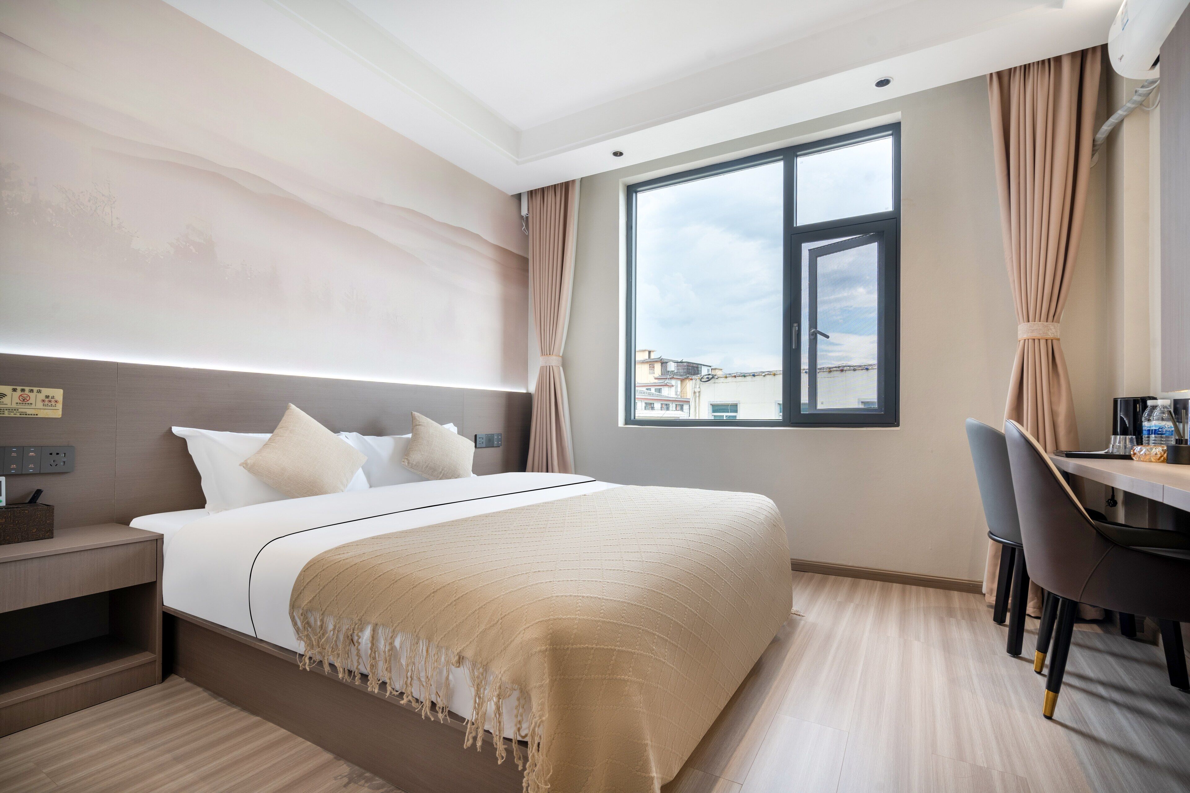 A hotel room with a large bed, a desk, and a view of buildings through a window.