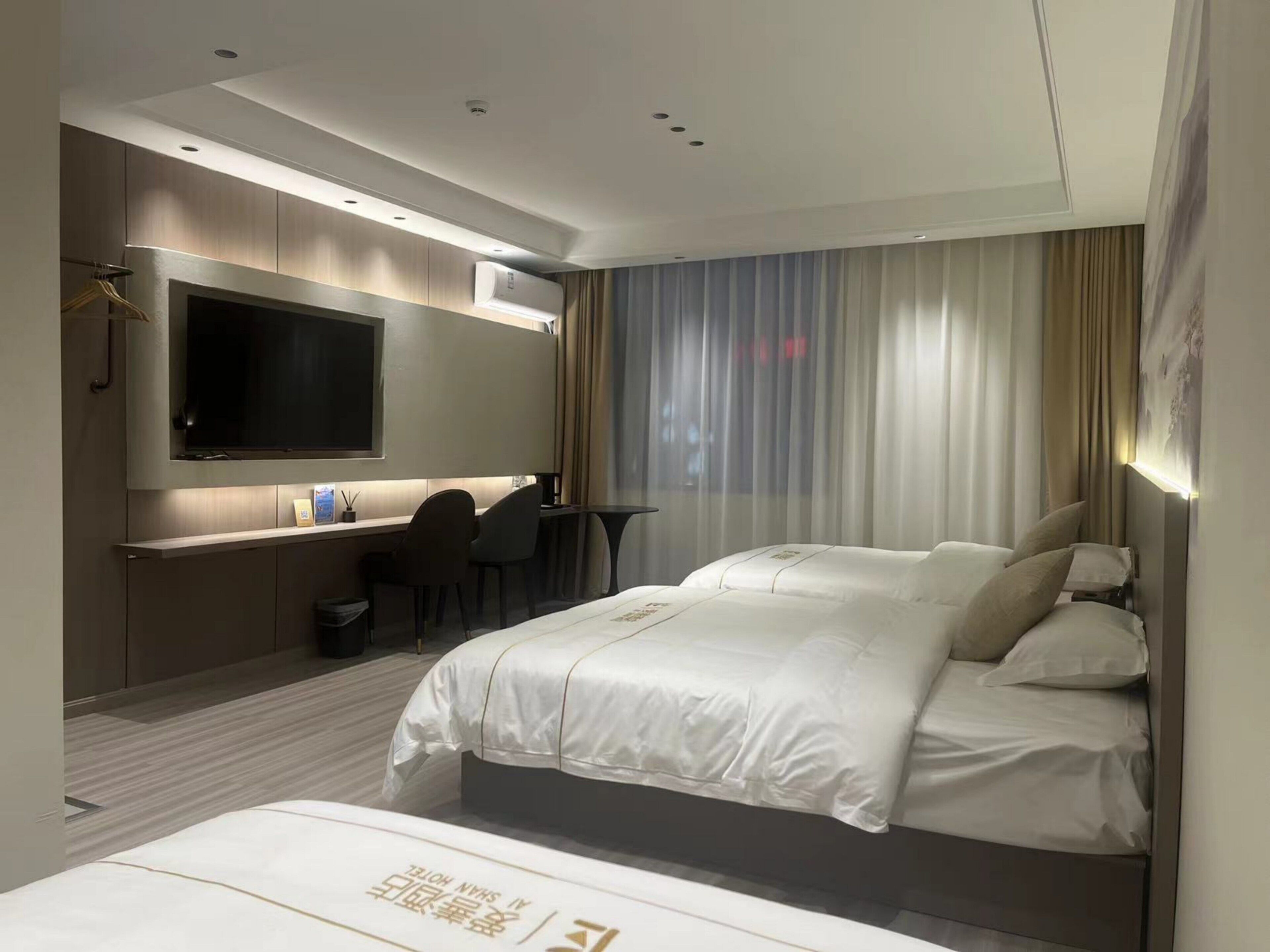 A hotel room with a large bed, a desk with a chair, a flat-screen TV, and a window with curtains.
