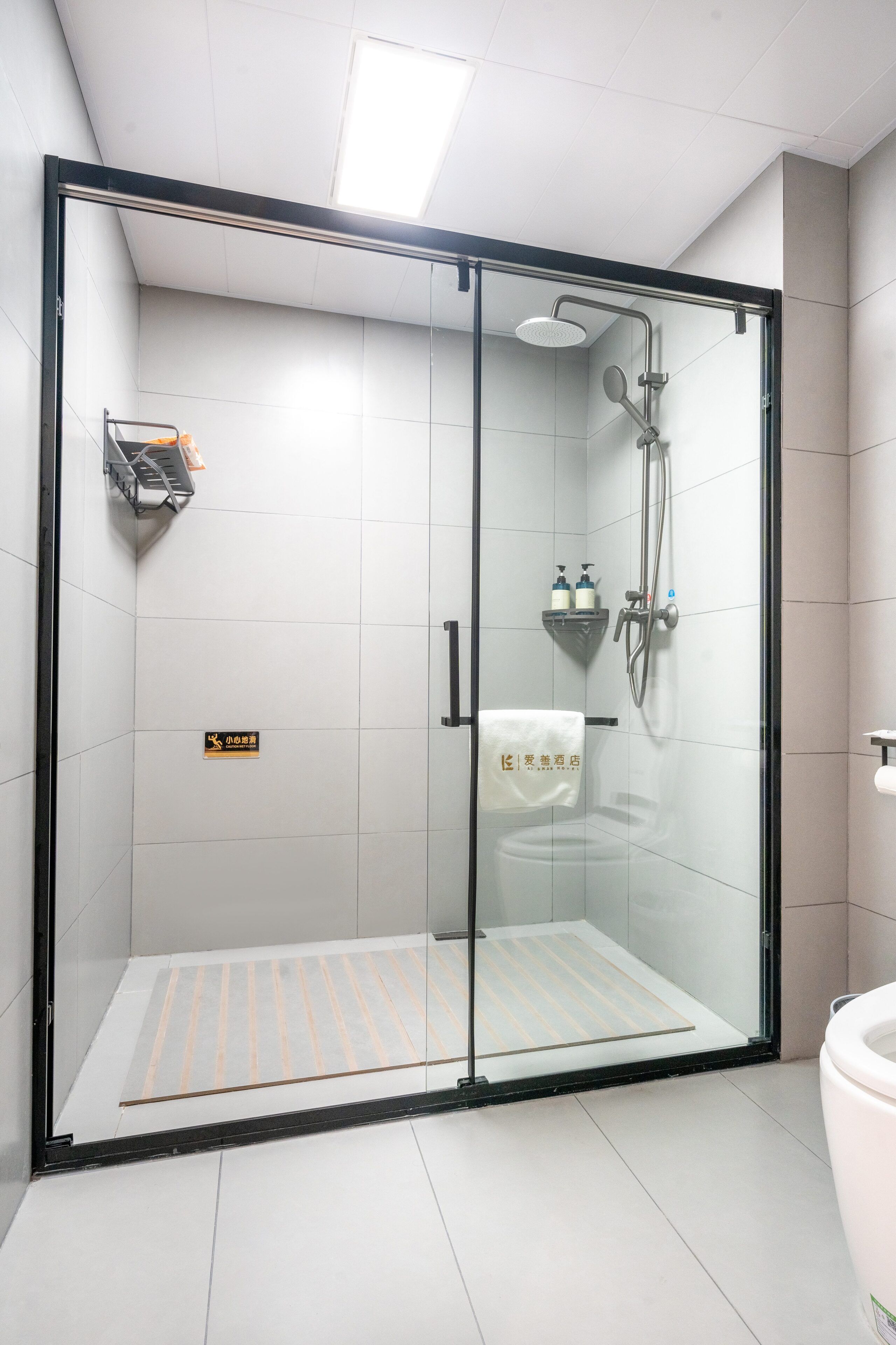 A glass-enclosed shower area with a white tiled floor, a towel rack, and a small shelf with toiletries.
