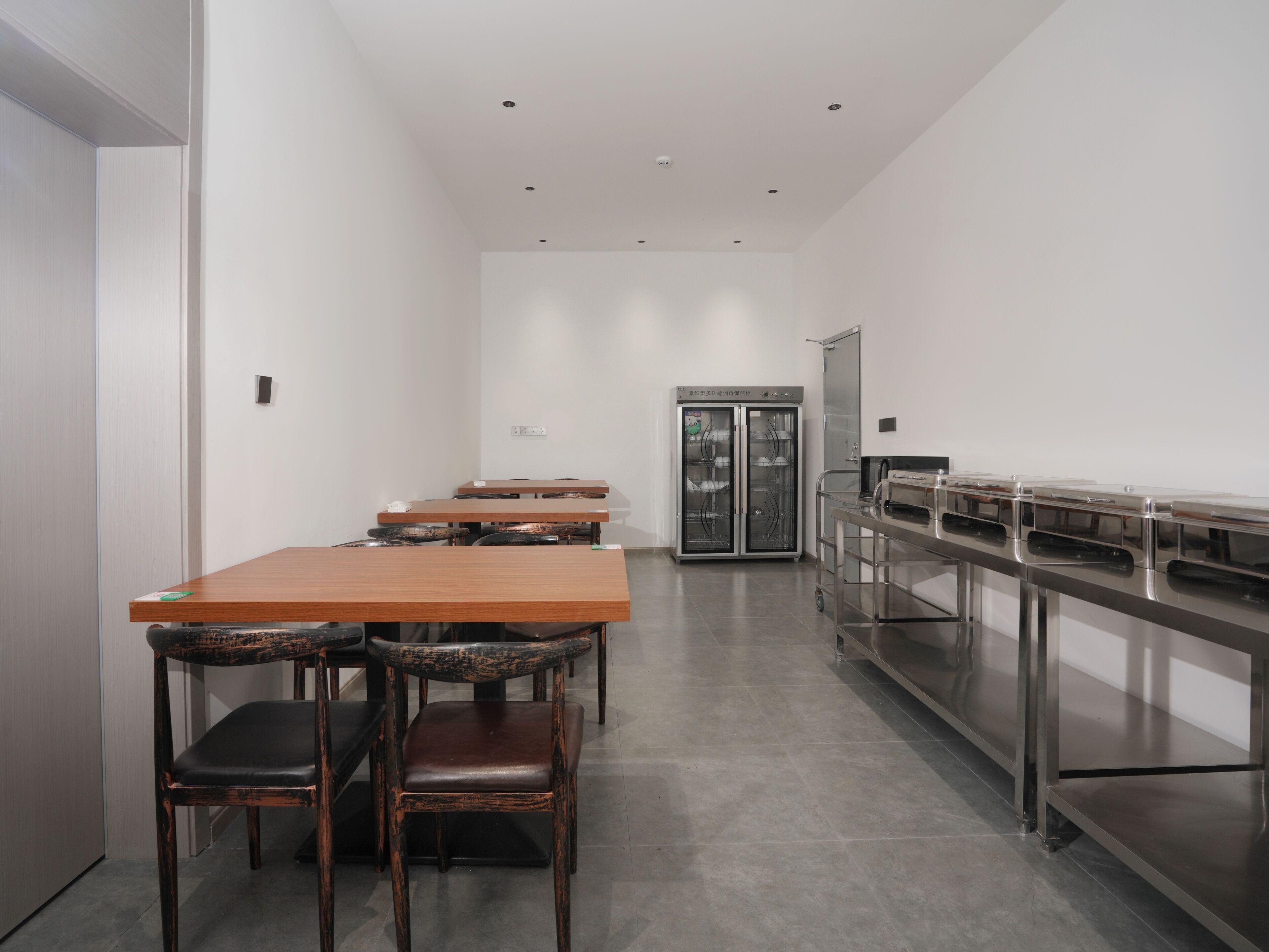 A modern dining area with a long wooden table and chairs, a stainless steel buffet counter, and a refrigerator.