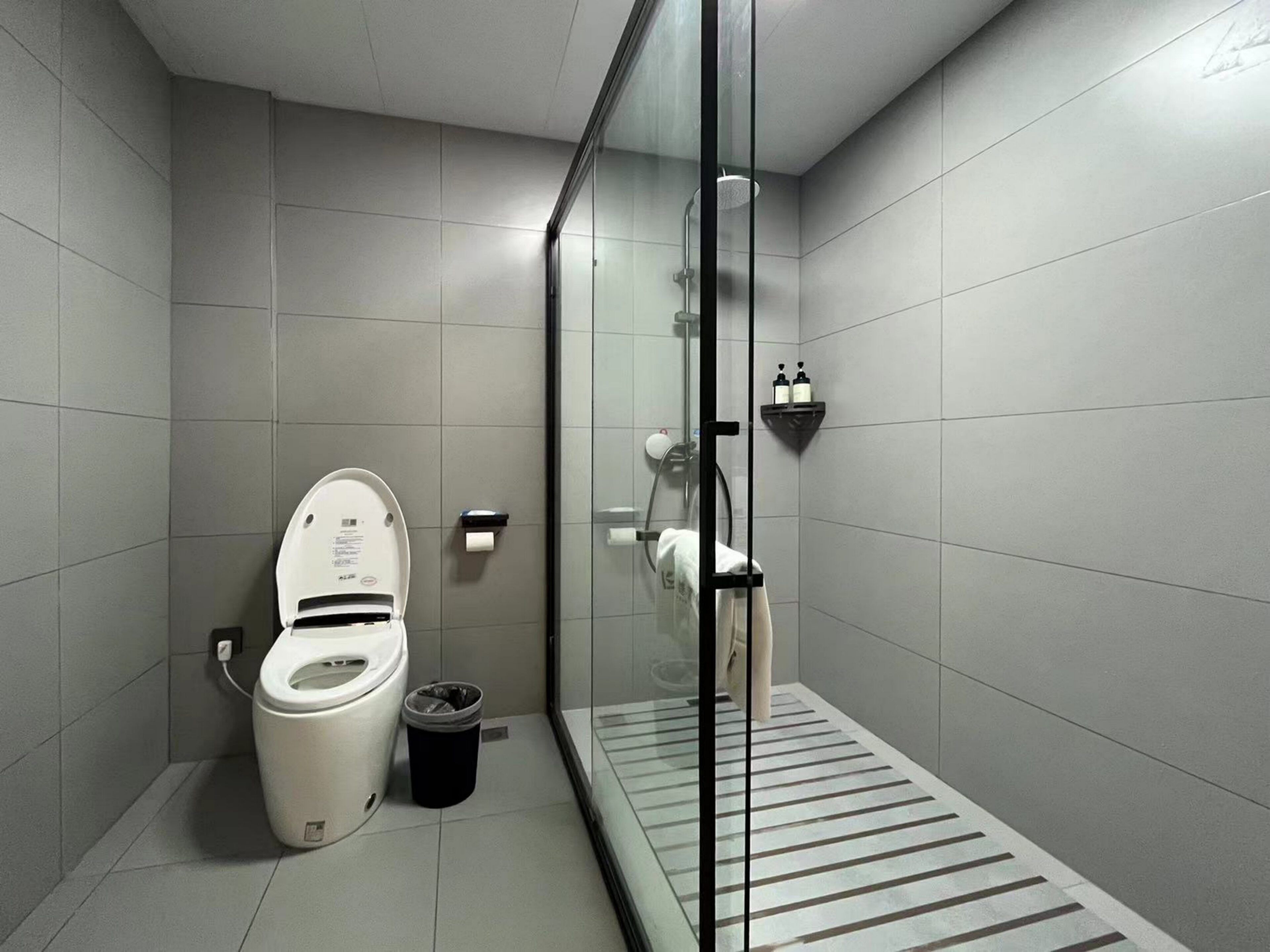 A modern bathroom with a toilet, a glass shower enclosure, and a small trash bin.