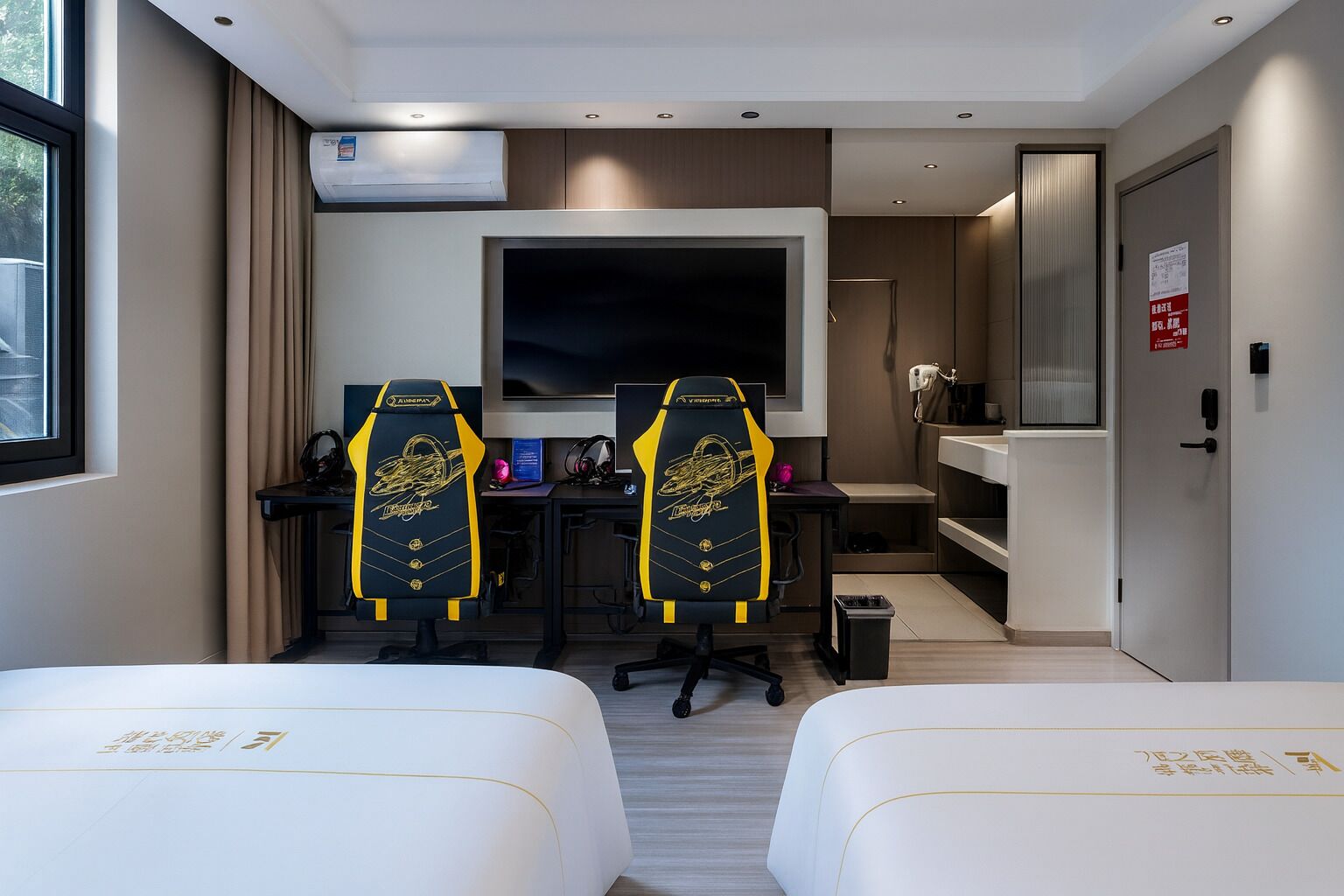 A hotel room with two beds, a desk with two gaming chairs, a TV, and a minibar.