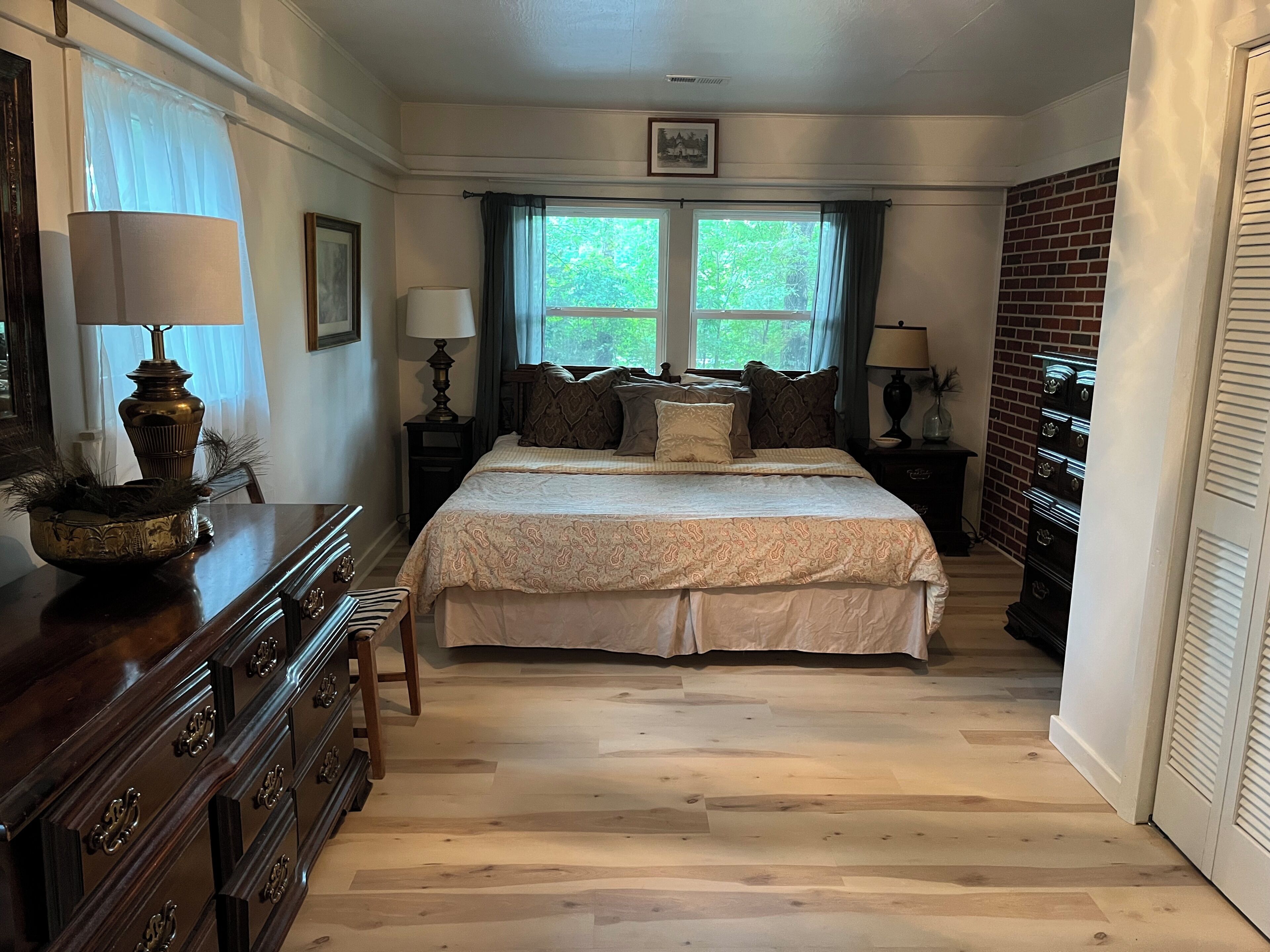 A bedroom with a large bed, two bedside tables with lamps, a dresser, and a window with curtains.