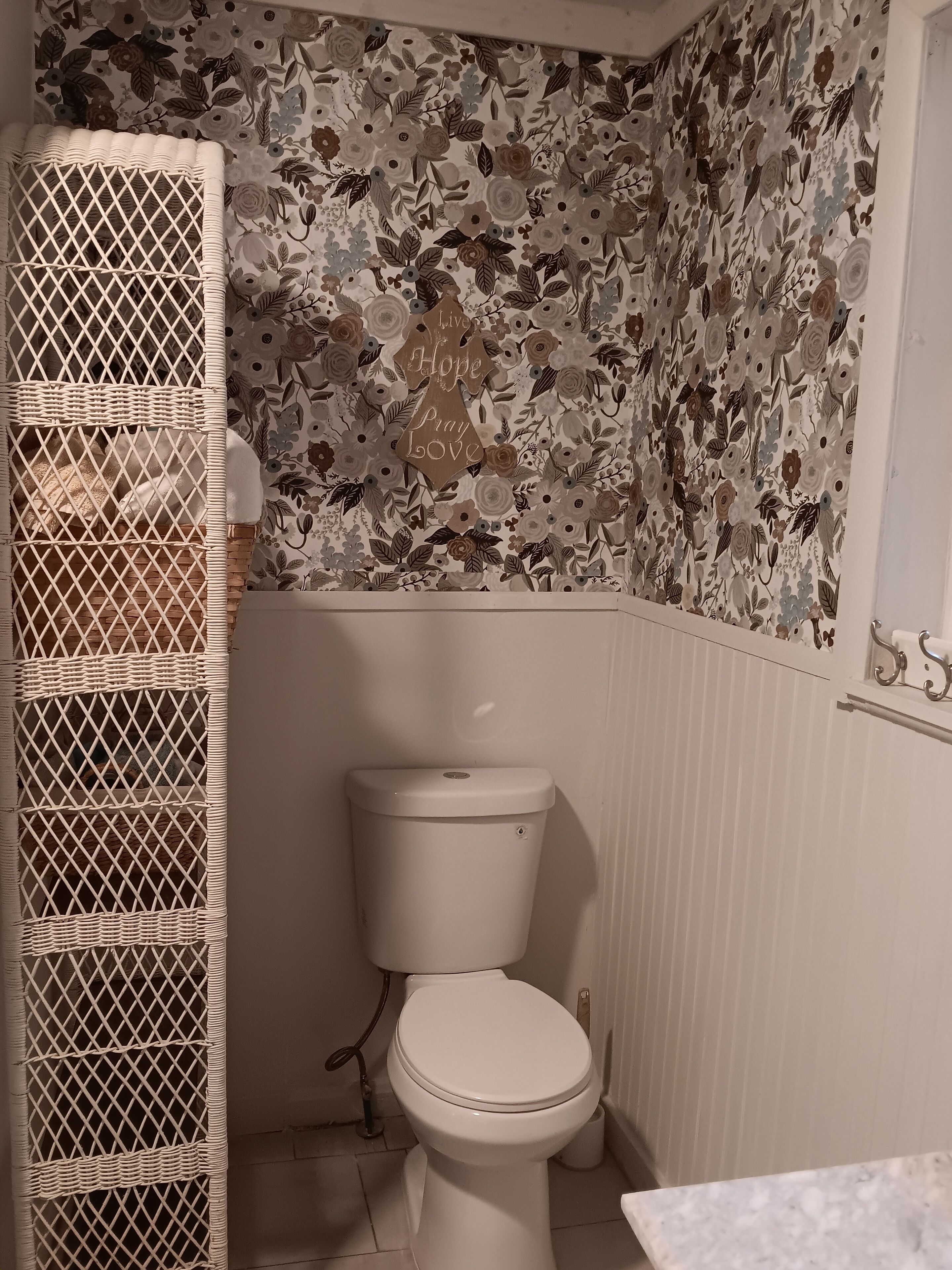 Casa de banho com sanita, cesto de vime e papel de parede floral.
