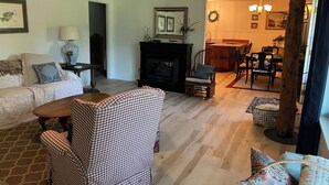 Una sala de estar con chimenea, un comedor con sillas de madera y una cocina visible a través de un vano abierto.