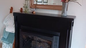 Une cheminée avec un manteau noir, un miroir au-dessus et un vase contenant des branches séchées sur le manteau.