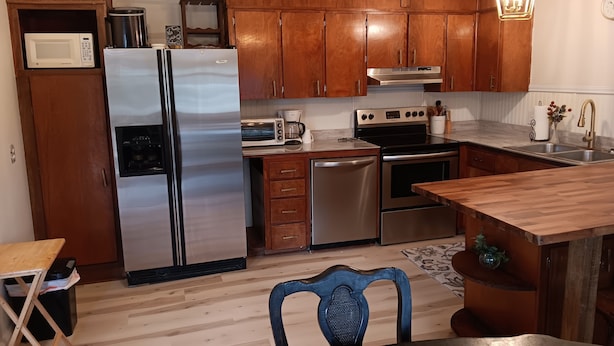 Une cuisine compacte dotée de meubles en bois, d’appareils électroménagers en acier inoxydable et d’un coin repas avec une table et des chaises.