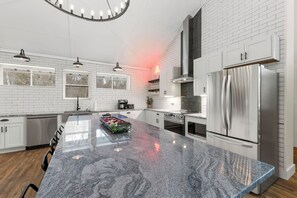 Une cuisine moderne avec des murs en briques blanches, des appareils électroménagers en acier inoxydable et un îlot central en granit.