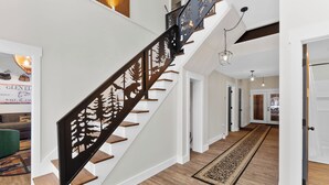 Una escalera con barandilla metálica decorativa, escalones de madera y una alfombra estampada en el suelo.