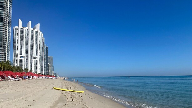Una playa con huellas, sombrillas rojas y edificios altos al fondo.