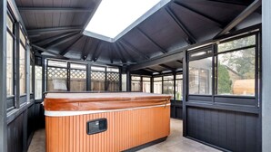 A hot tub in a covered outdoor area with a sloped ceiling and large windows. - Duplex|4Min Walk to NYC Train|Gameroom|Hotub+Sauna (Bayonne)