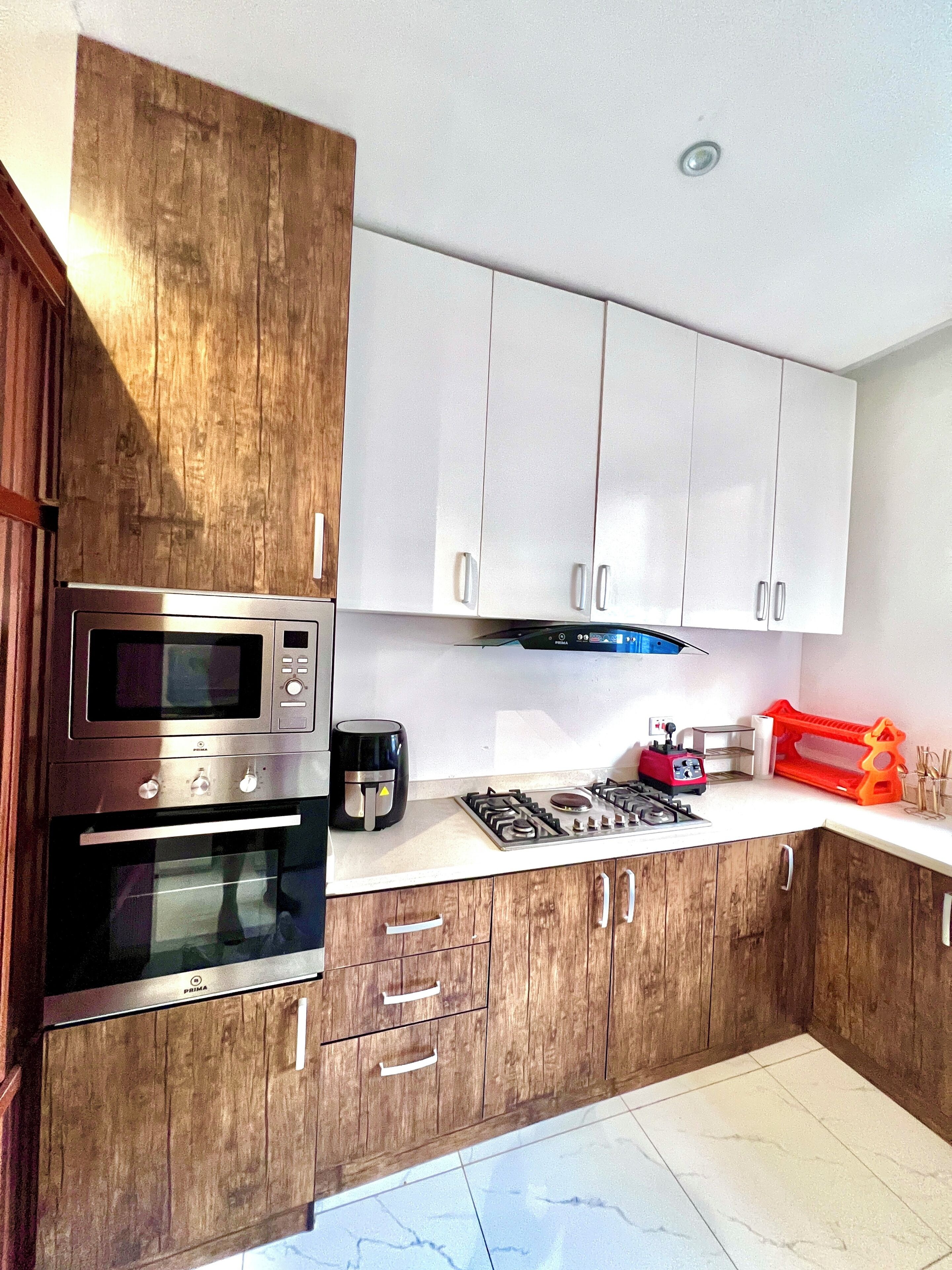 Une cuisine moderne avec des meubles en bois, des appareils en acier inoxydable et un plan de travail blanc.