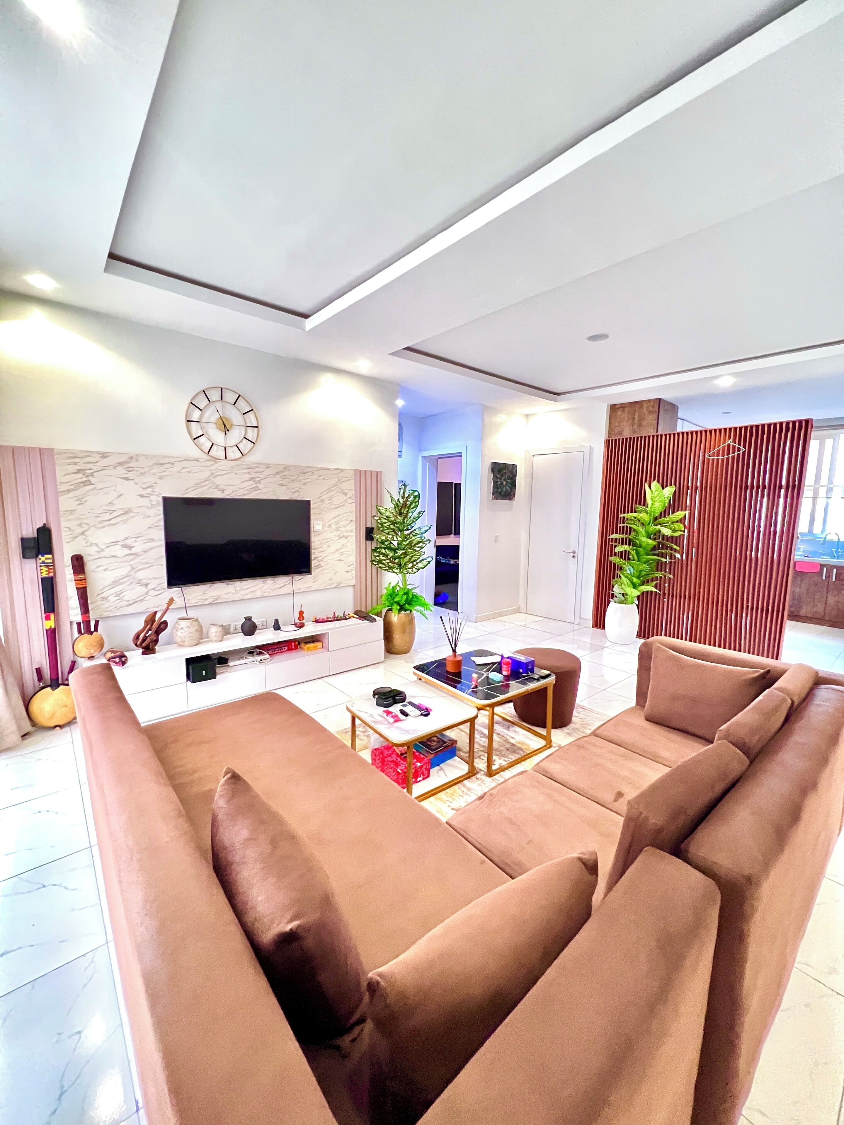 A modern living room with a large flat-screen TV, brown sofas, a coffee table, and decorative items.