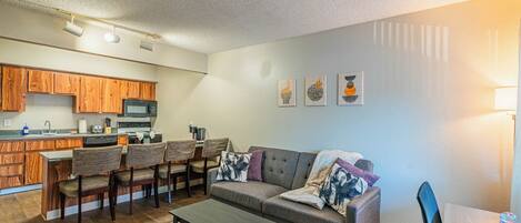 A modern living room with a grey sofa, wooden cabinets, and a kitchen area in the background.