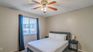A bedroom with a bed, a nightstand, a ceiling fan, and a window with curtains.