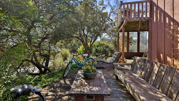 Une terrasse extérieure en bois avec un vélo, un banc et une table agrémentée d’une plante.