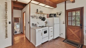 Une cuisine compacte avec des meubles blancs, un four encastré, un micro-ondes et des casseroles suspendues.