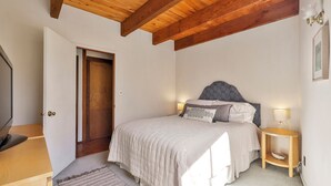 Une chambre avec un plafond en bois, un lit doté d’une tête de lit à motifs, des lampes de chevet et une petite table de chevet.