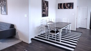 Ein modernes Wohnzimmer mit einem grauen Sofa, einem Esstisch mit weißen Stühlen und schwarz-weißen Teppichen.