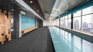 A modern indoor swimming pool with a city view, wooden benches, and a clear ceiling. - Spacious landmark in the heart of Mel CBD (Melbourne)