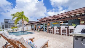 A poolside area with lounge chairs, a barbecue grill, and a bar with outdoor seating. - Waterfront Retreat With Pool Tiki Bar Boat Dock (Palm Coast)