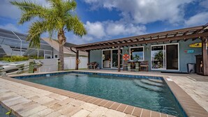 A swimming pool with a covered patio area, palm trees, and a building with a sign that reads "The Bar". - Waterfront Retreat With Pool Tiki Bar Boat Dock (Palm Coast)