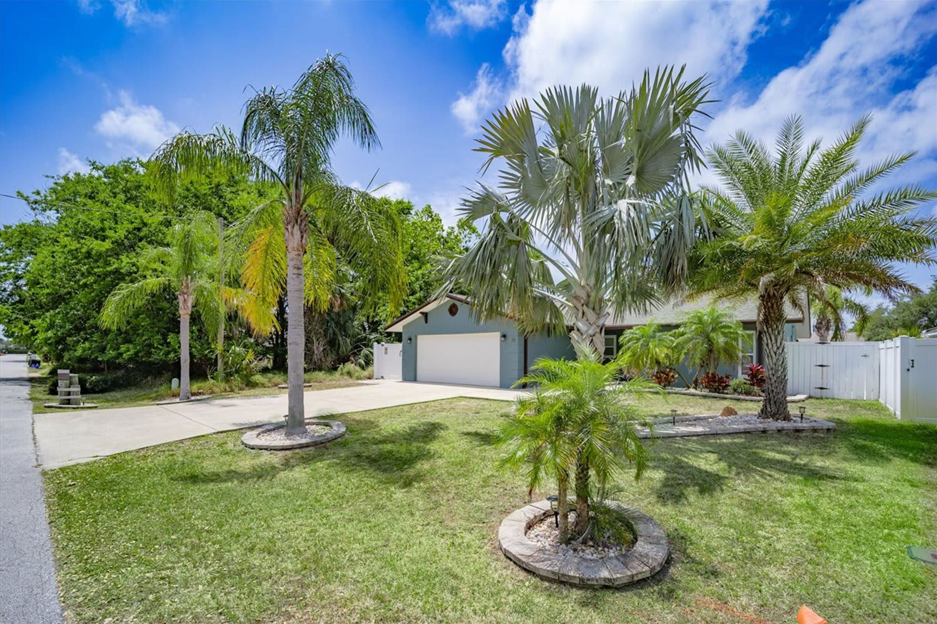A residential property with a well-maintained lawn, palm trees, and a garage.
