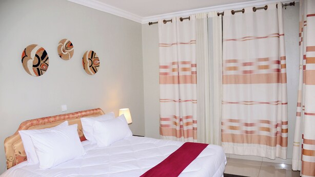 A neatly made bed with white bedding and a red accent, a wall with three decorative wall art pieces, and a window with striped curtains.