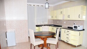 A compact kitchen with a round dining table, two chairs, a refrigerator, a microwave, and yellow cabinets.