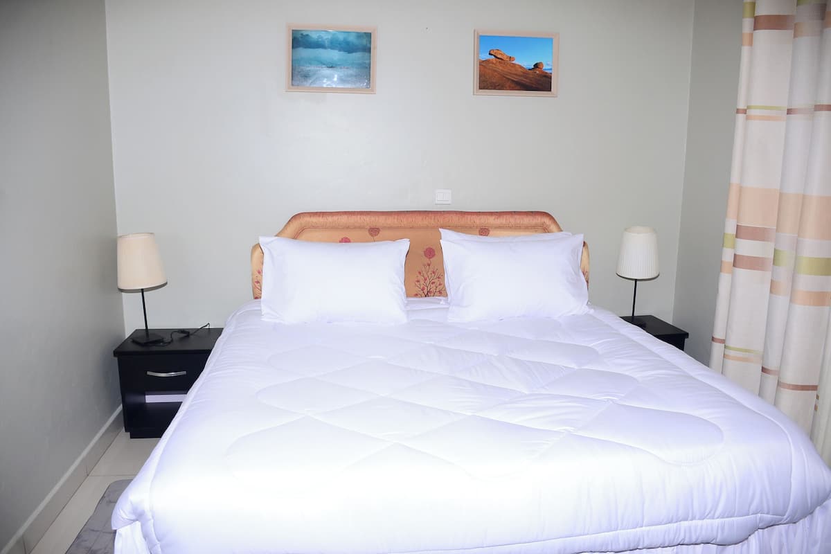 A neatly made bed with white bedding, two bedside tables with lamps, and two framed pictures on the wall.