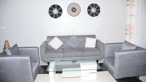 A modern living room with a grey sofa set, a glass coffee table, and decorative wall art.