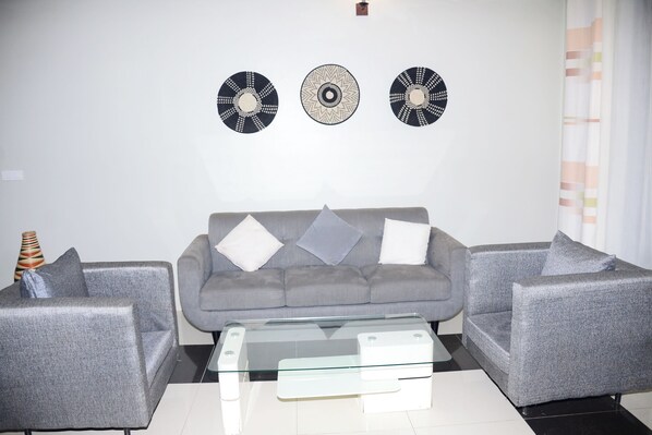 A modern living room with a grey sofa set, a glass coffee table, and decorative wall art. - Konvine Boutique Hotel (Kigali)