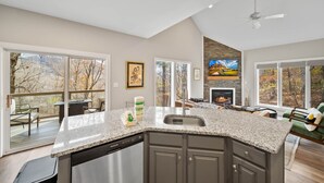 A spacious kitchen with a large island, a dining area with a fireplace, and a deck with outdoor seating. - Cozy Cottage in Yonahlossee Racquet Club (Boone)