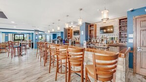 A bar area with wooden bar stools, a counter with a variety of bottles, and a television mounted on the wall. - Rare find! Ocean front bedroom, Pet friendly! (Myrtle Beach)