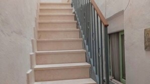 Una escalera estrecha con escalones color beige y barandilla de metal, que lleva a un ventanal con marco verde.