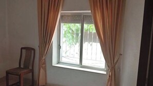 Una habitación con ventana, cortinas, una silla y suelo de baldosas.