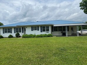 A single-story house with a blue roof, a covered porch, and a well-maintained lawn. - Spacious 7-bedroom farmhouse in peaceful Montgomery City with AC (Montgomery City)