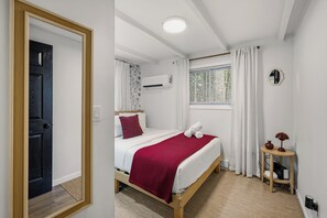 A bedroom with a bed, a bedside table, an air conditioning unit, a window with curtains, and a door. - Summit Home - The Ultimate Summit of Style for 12 (Tobyhanna)