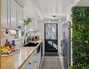 A modern kitchen with white cabinets, a wooden countertop, a black backsplash, and a green vertical garden. - Summit Home - The Ultimate Summit of Style for 12 (Tobyhanna)