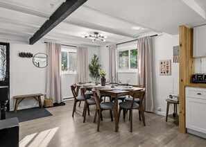 A dining area with a wooden table set for six, surrounded by chairs, in a room with large windows and a view of greenery outside. - Summit Home - The Ultimate Summit of Style for 12 (Tobyhanna)