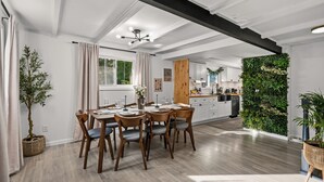 A modern kitchen with white cabinets, a wooden dining table, and a green vertical garden.