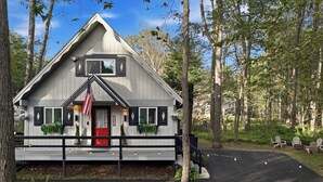 A cabin with a red door, black shutters, and a small porch with potted plants.