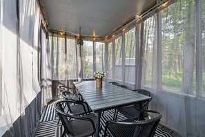 A covered outdoor dining area with a table and chairs, a vase with flowers, and a view of trees through the windows. - Summit Home - The Ultimate Summit of Style for 12 (Tobyhanna)